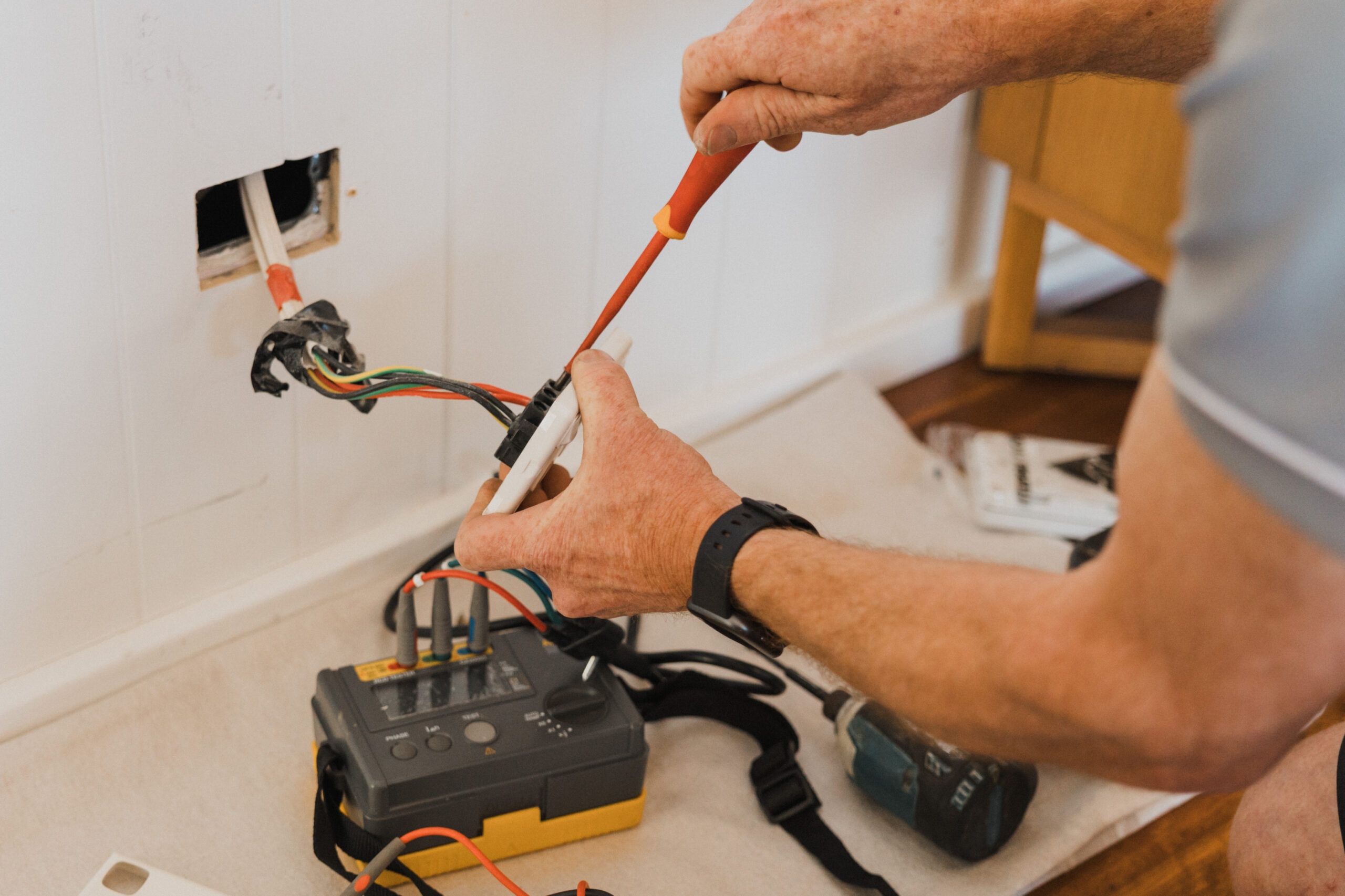 Electrician inspecting a detached electrical socket with a testing tool during a home electrical safety check in Sydney